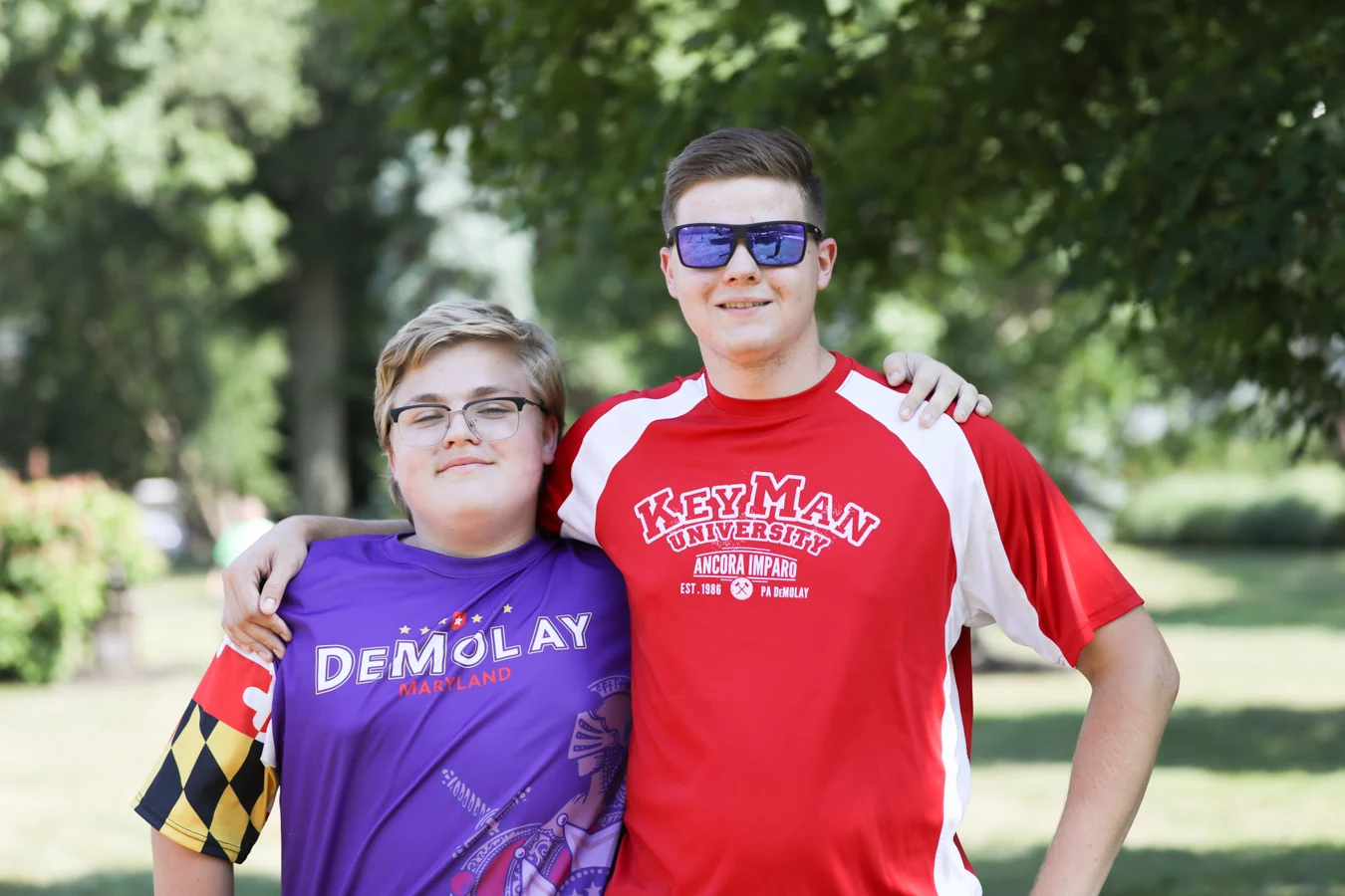 Two smiling teen boys outdoors with arms around each other.