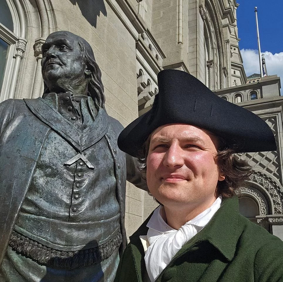 542756832_10240451984063099_2064075810207564057_n Man in Colonial-era costume with Benjamin Franklin statue and front of the Masonic Temple behind him.