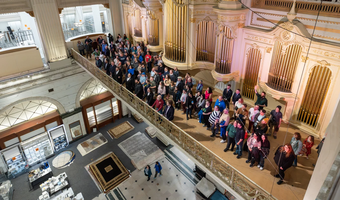 9I4A0964-Enhanced-NR Group of men and women standing in hallway with ornate Wanamaker Building organ pipes behind them.