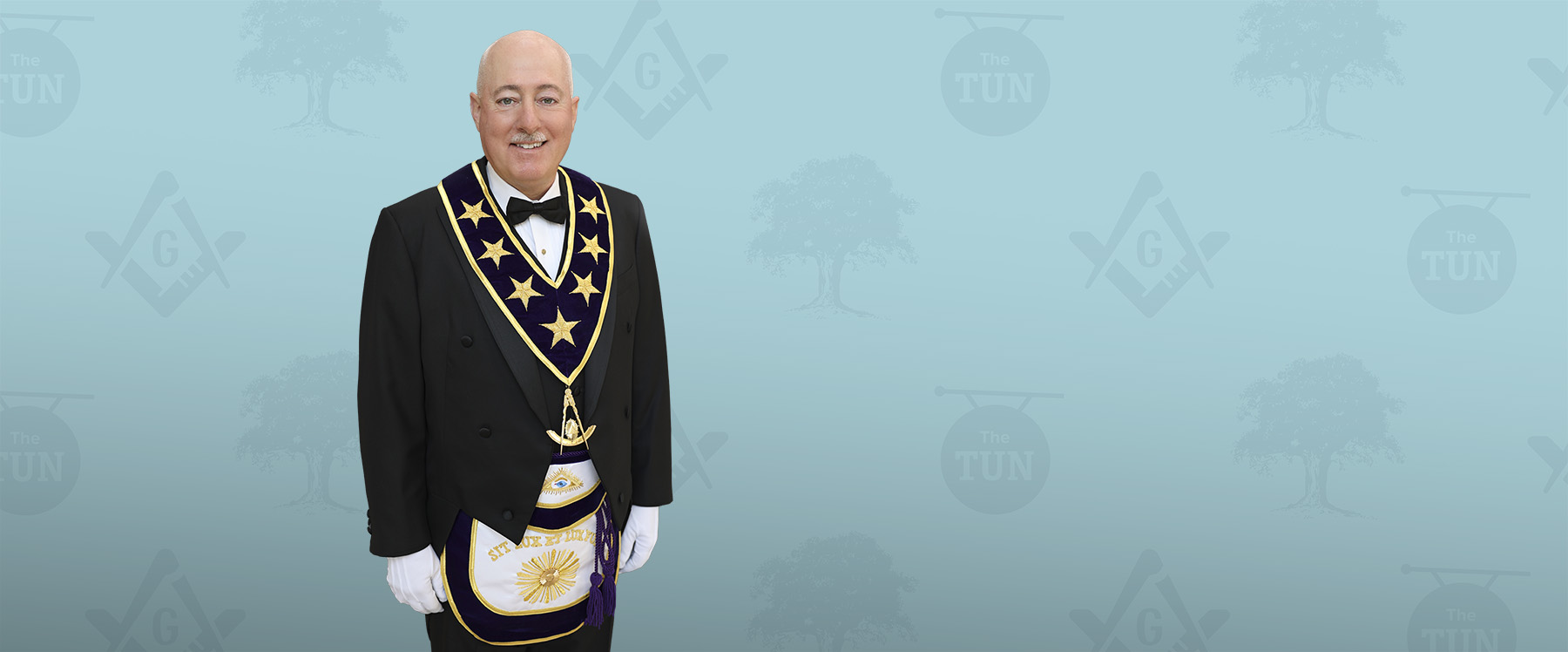 Brink_Photobackdrop_2025 v3.81 Portrait of R.W. Grand Master Robert Brink in Masonic attire against a blue patterned background.