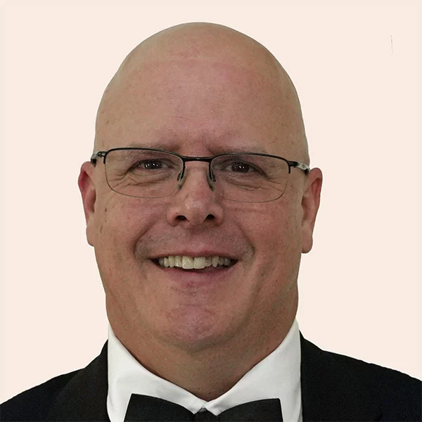 Smiling man wearing glasses, suit and bow tie.