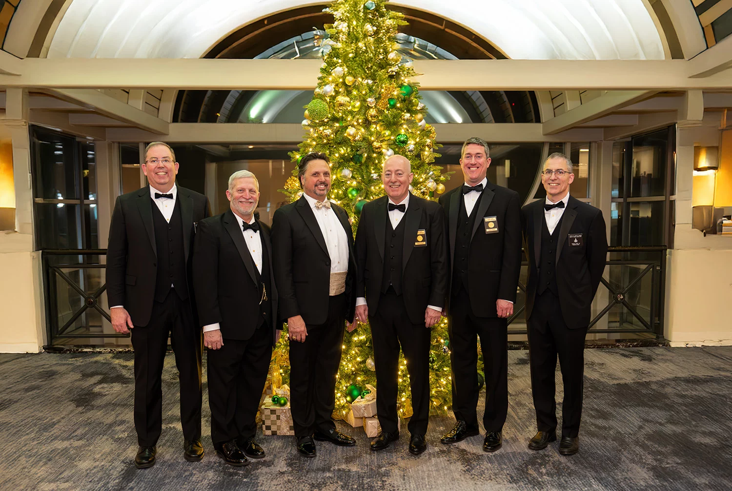 Grand Lodge Officers in formal attire smiling while standing in front of a lit Christmas tree,