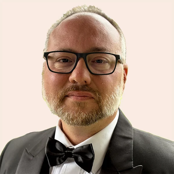 Man with black glasses, short hair and beard wearing a suit and bowtie.