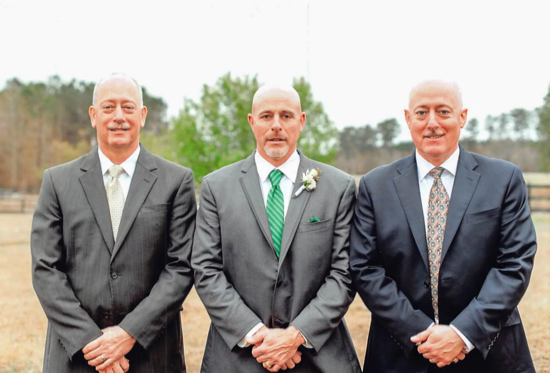 Three smiling men in suits standing outdoors.