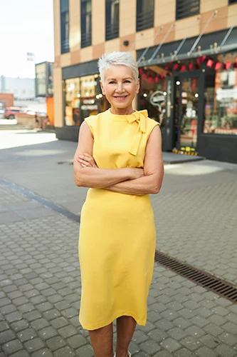 Smiling woman outdoors in knee-length yellow dress.