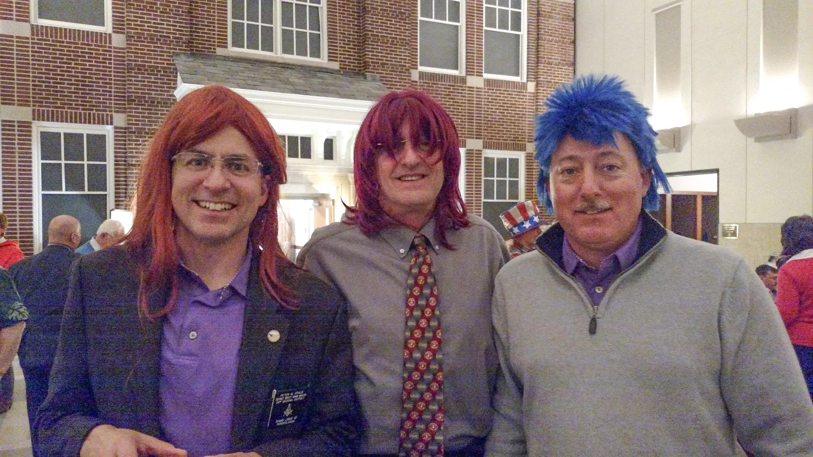 Three smiling men wearing colorful wigs.