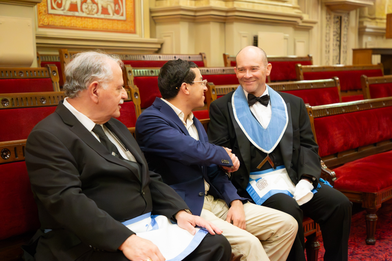 IMG_9860 Masons sitting and shaking hands with prospective member in lodge room.