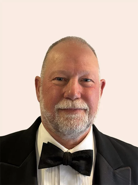 Smiling man with short grey hair and beard wearing a suit and bow tie.
