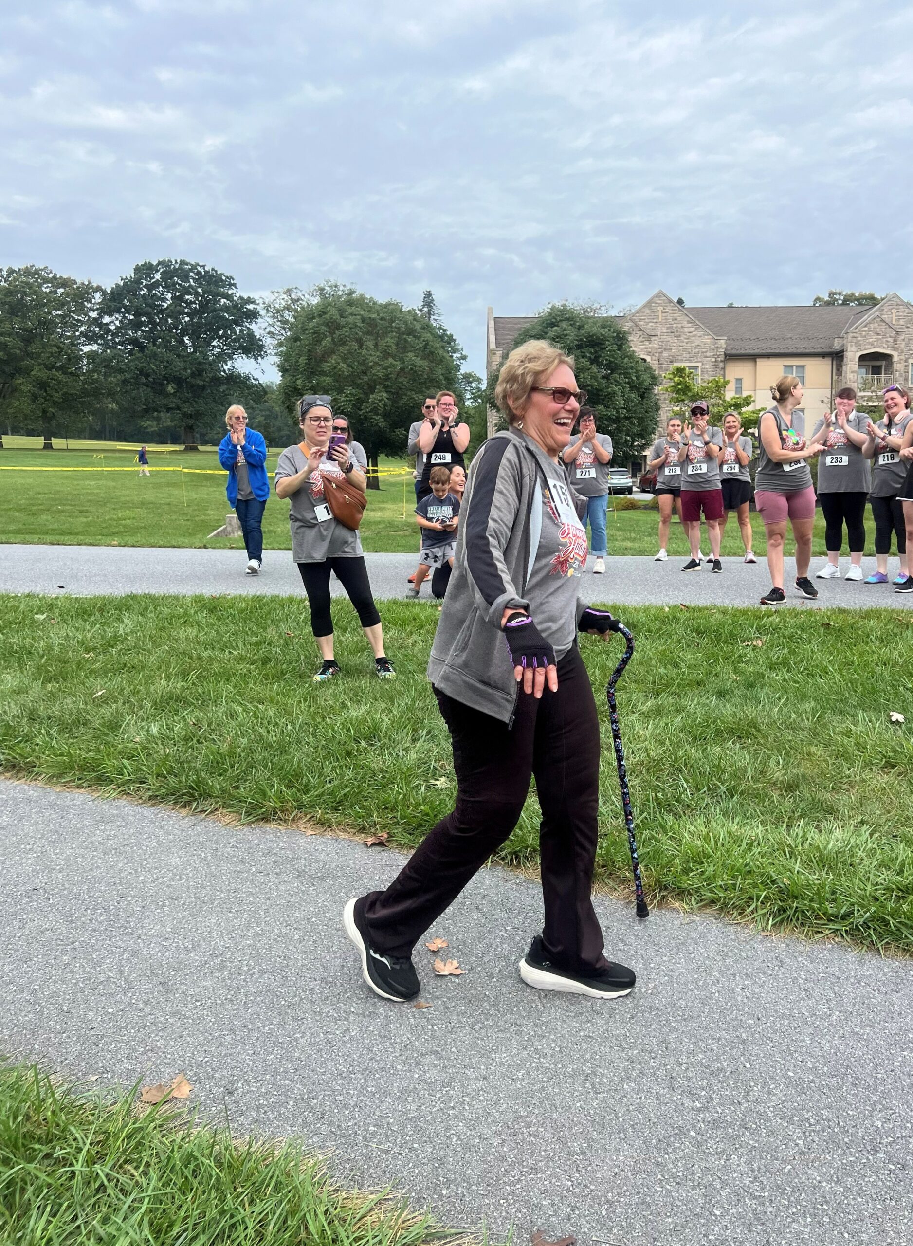 Smiling woman walking with cane while crowd applauds in the background.