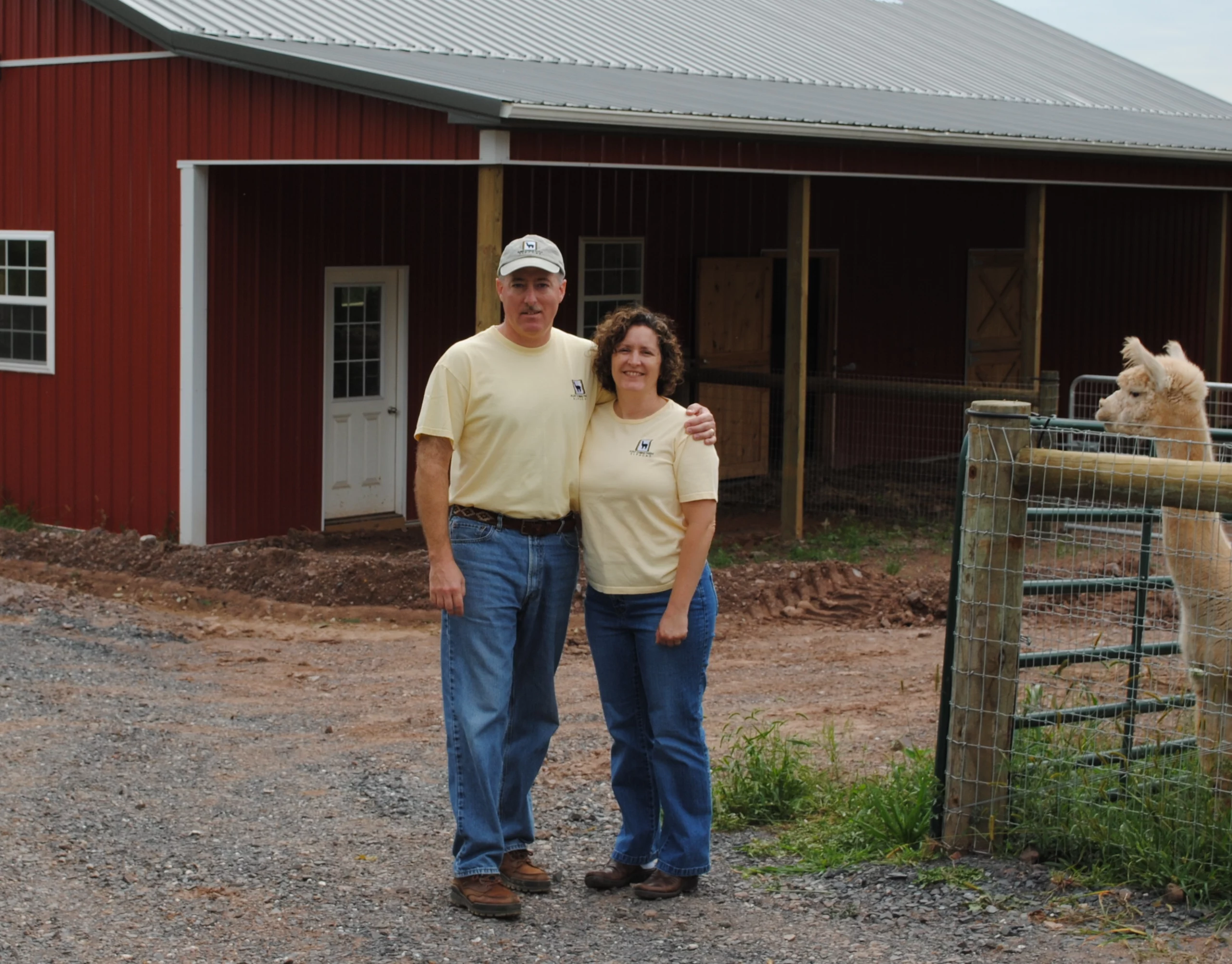 Grand Master Robert Brink with his arm around his wife, standing outside of red barn and surrounding farm.