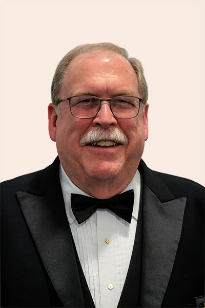Smiling man with short hair and mustache wearing glasses and suit with a bowtie.