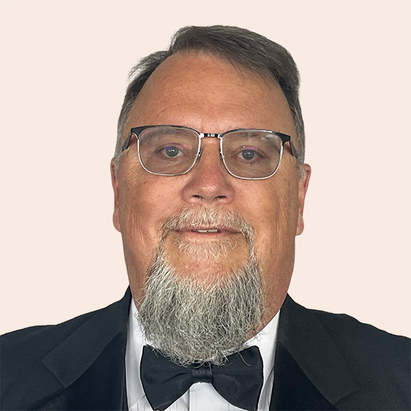 Timothy C Dedman DDGM03_PNG_nobackground Smiling man with short grey hair and goatee wearing glasses, a bowtie and suit.