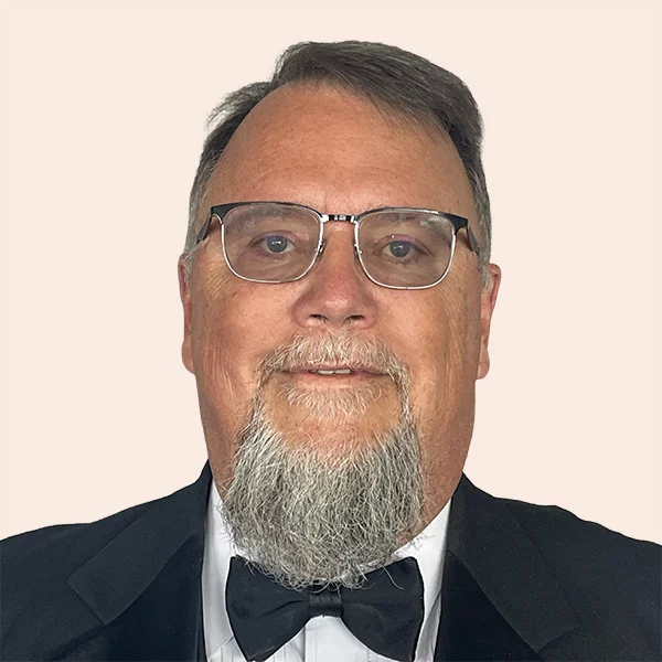 Smiling man with short grey hair and goatee wearing glasses, a bowtie and suit.