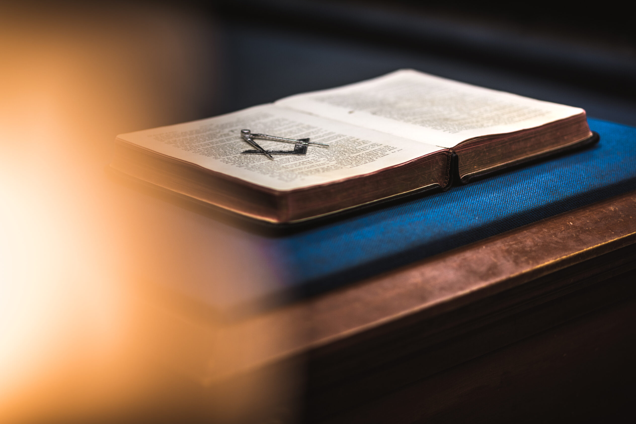 Bible laying open with metallic Square and Compasses laying on top of the pages.