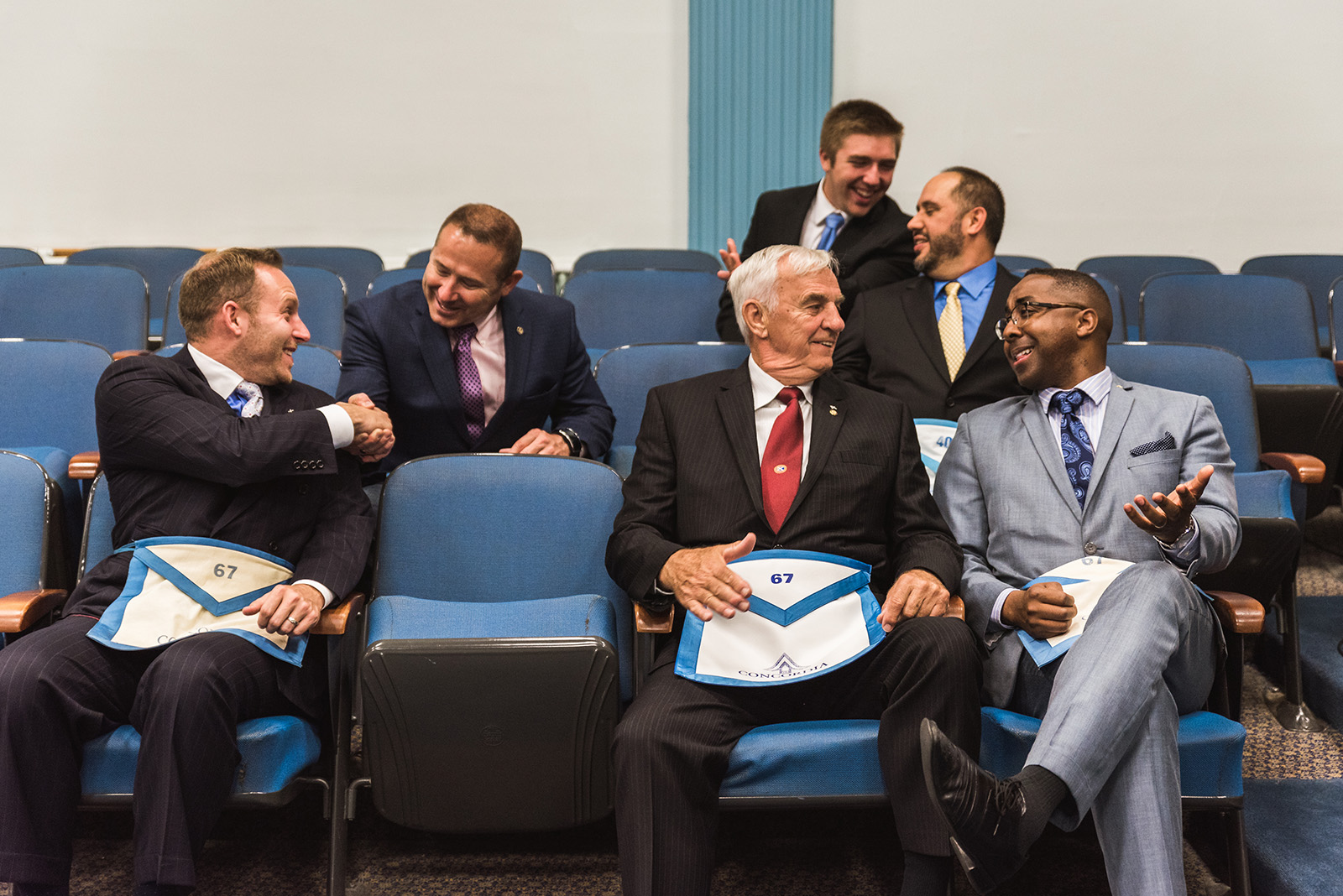 Men in Masonic dress shaking hands while seated on a bench.