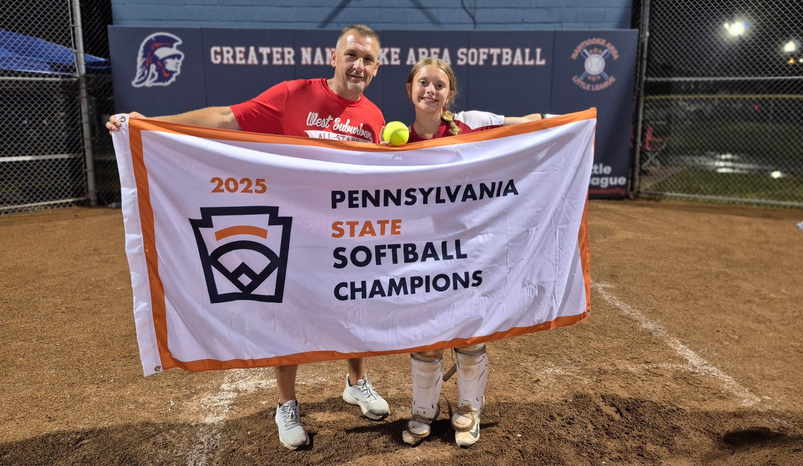 Smiling man and girl holding up a banner on a baseball field. The banner reads, "2025, Pennsylvania State Softball Champions."