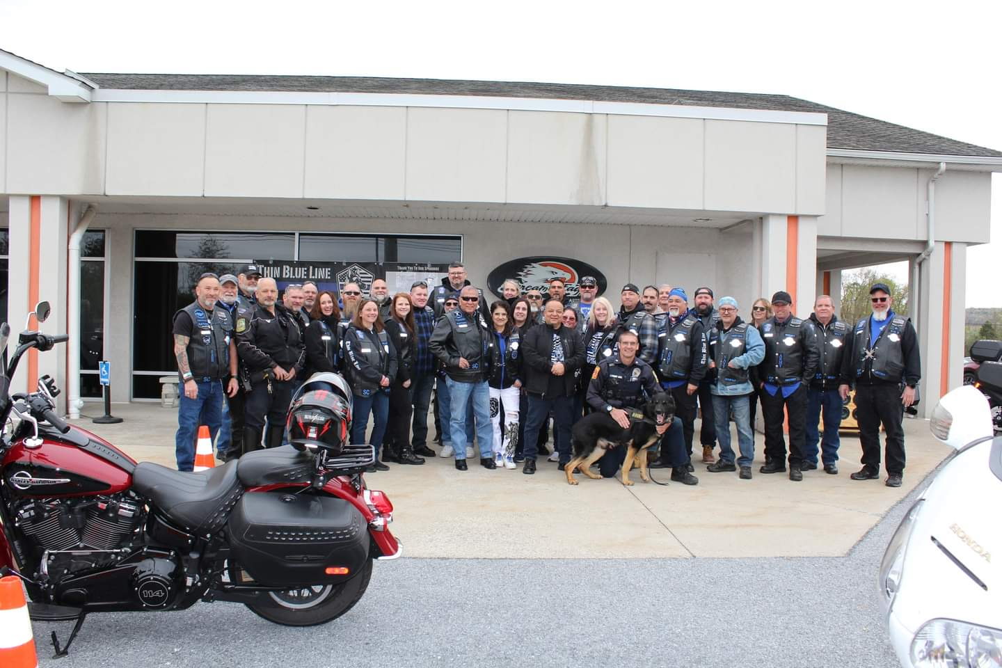 Group of people in vests, police officer and his dog stand in front of the group.