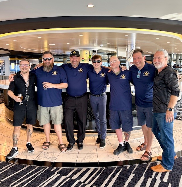 Smiling group of men standing together inside room on a ship.