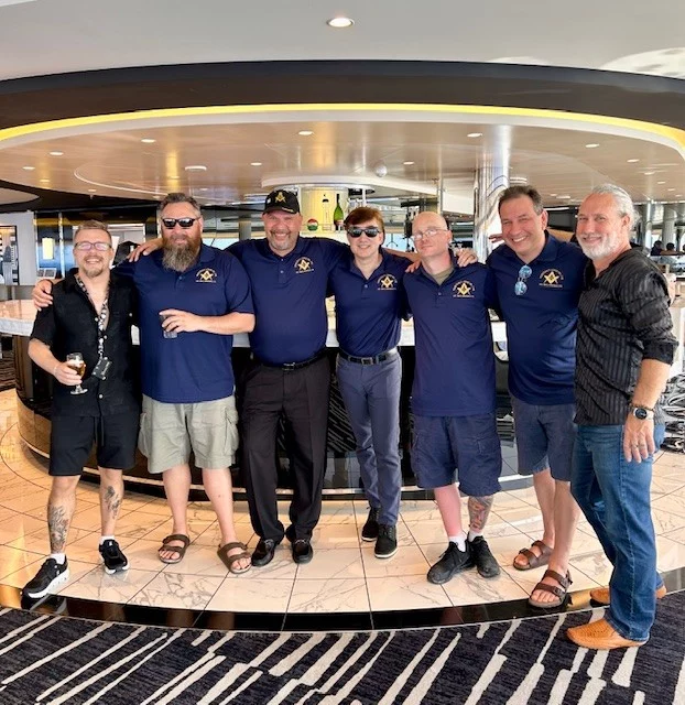 Smiling group of men standing together inside room on a ship.