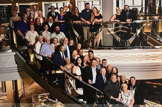 Large smiling group of smiling men and women standing on landing and staircase.