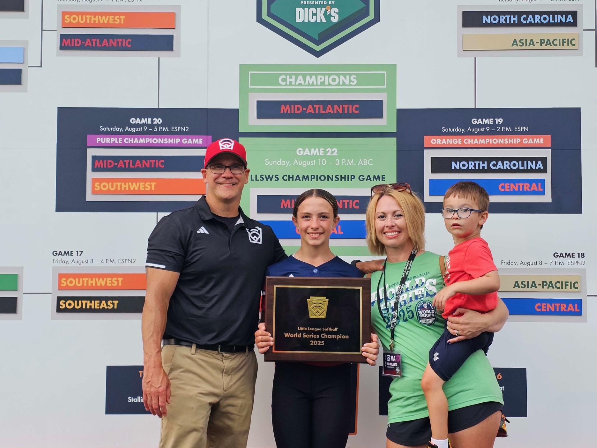 Smiling family, including a man, woman, girl and young boy, standing in front of ESPN Big Bracket signage. The girl is holding up a plaque.