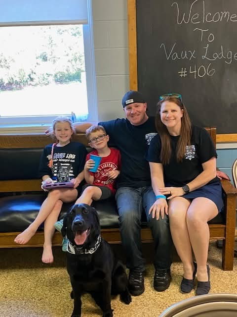 Smiling family seated on a bench with their black lab seated in front of them.
