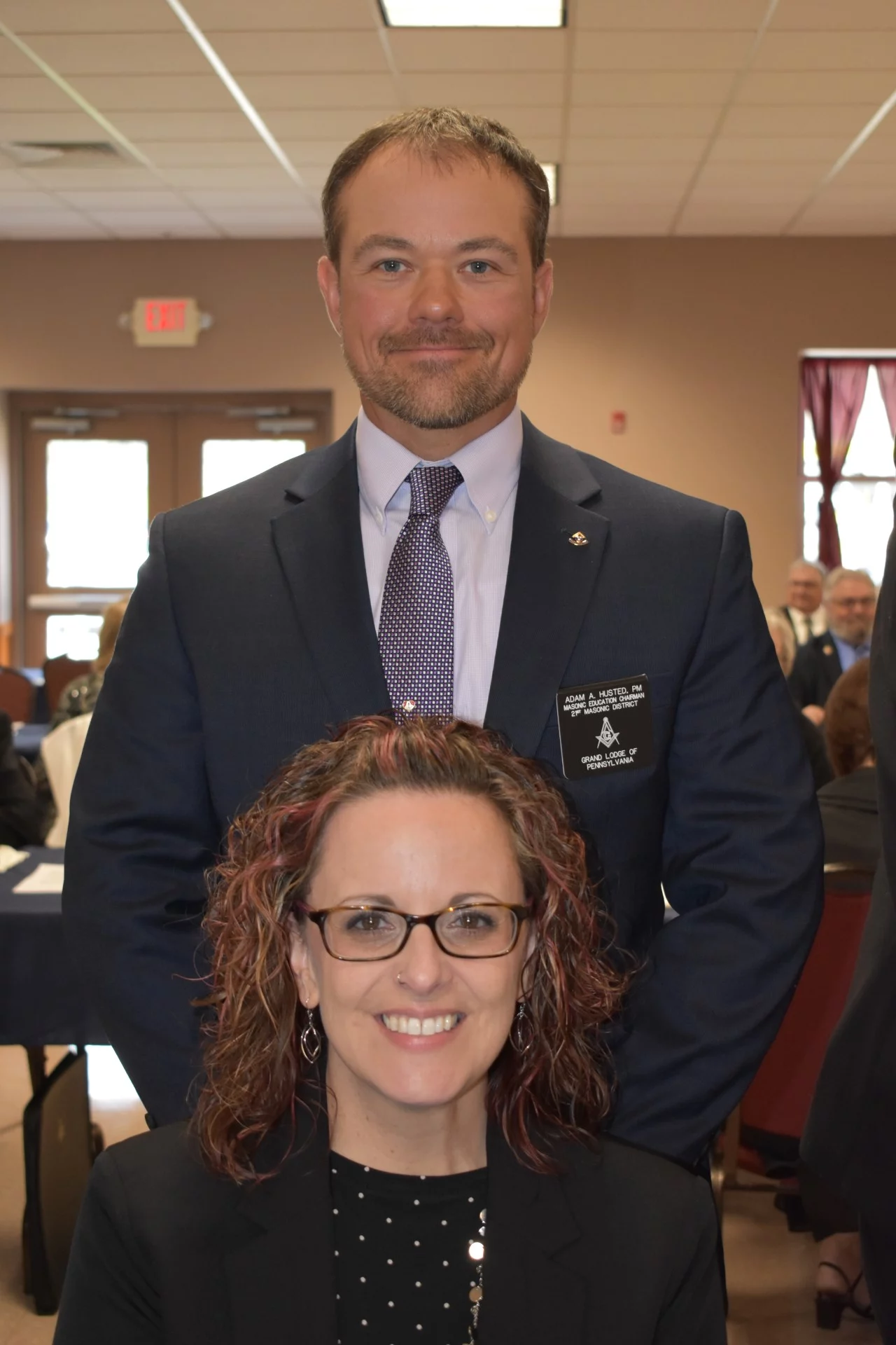 adam husted photo A smiling woman seated with her husband standing behind her. Both are dressed formally.
