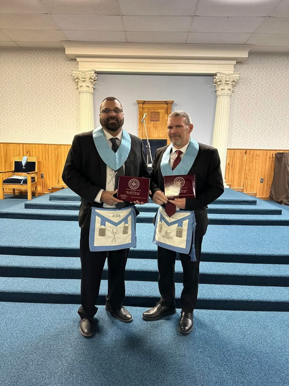 Two smiling men in Masonic dress holding up plaques.