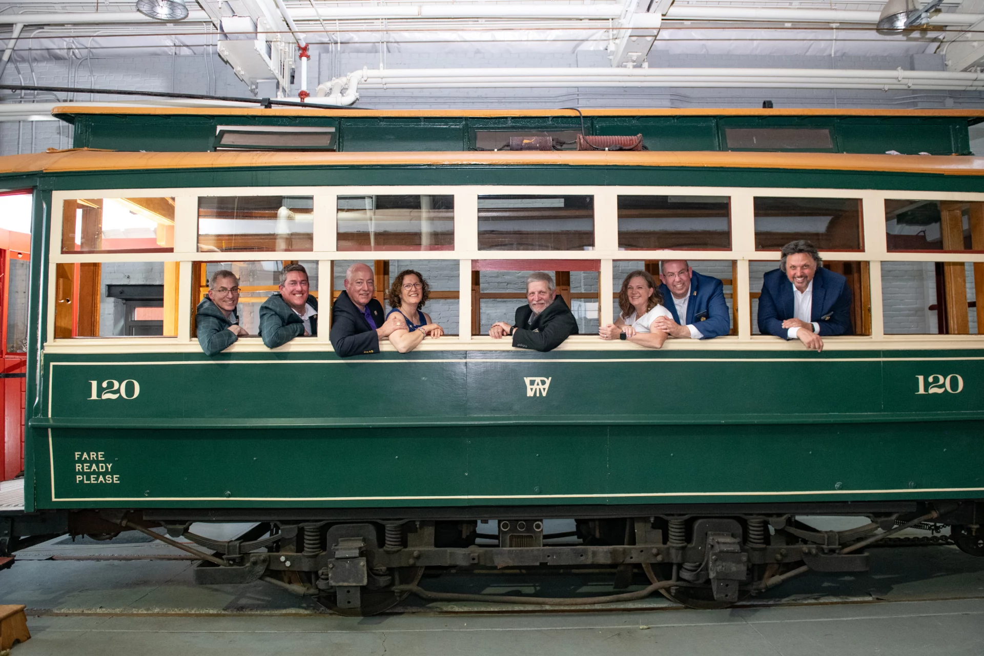Smiling group of Grand Lodge officers and two of their wives seated in a green train car together.