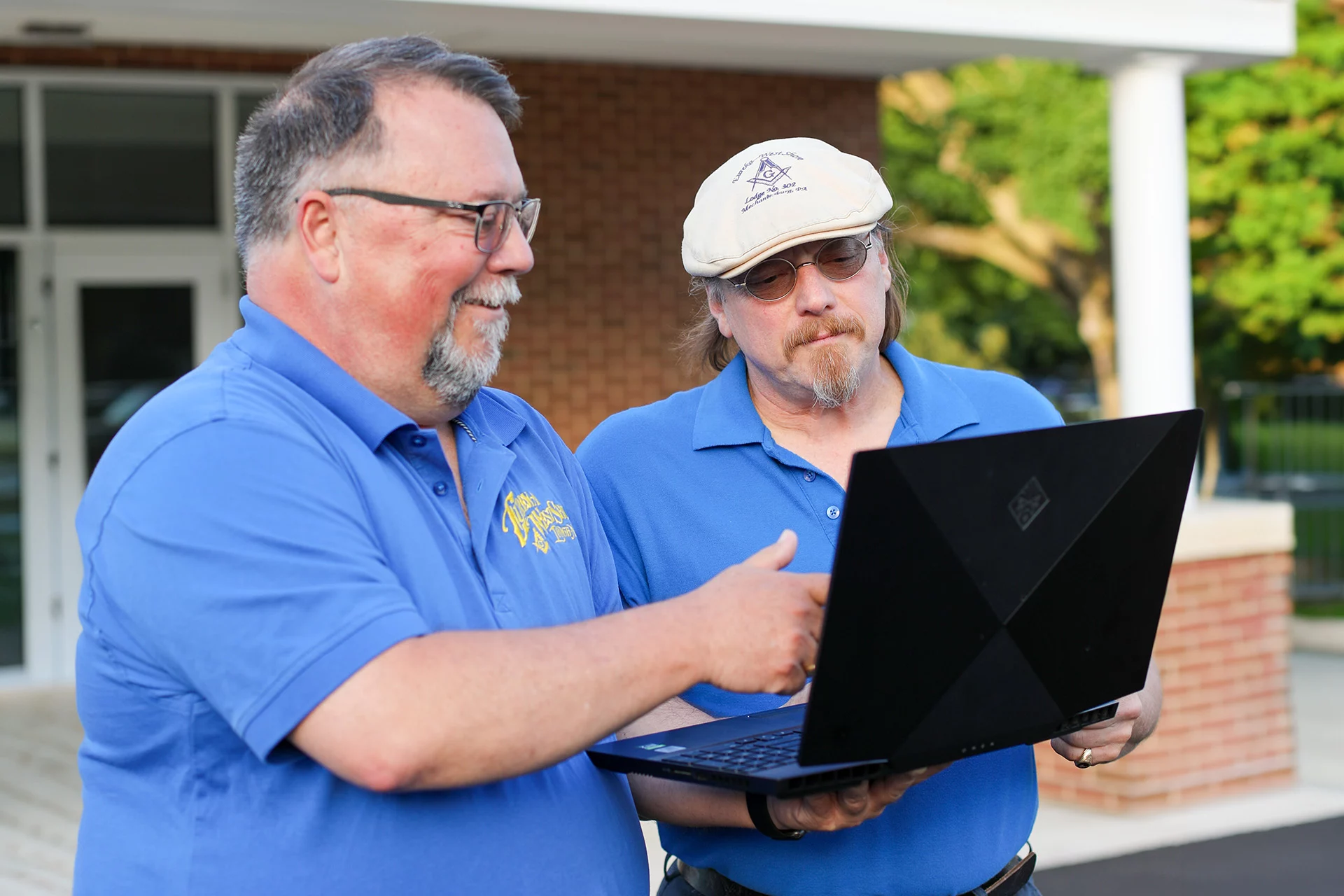 Smiling men looking at laptop computer together outdoors.