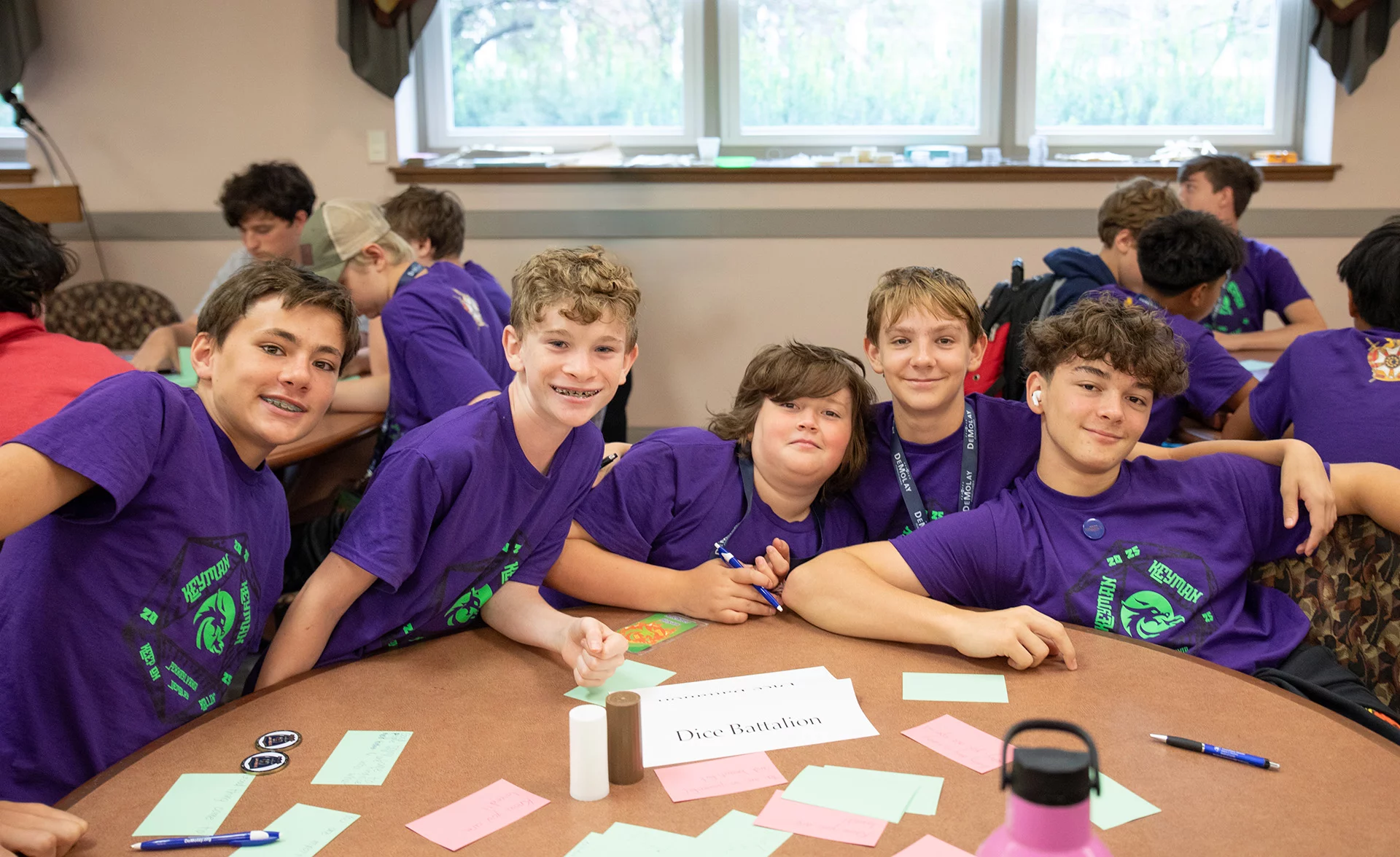 Smiling group of boys in purple shirts seated around a table.
