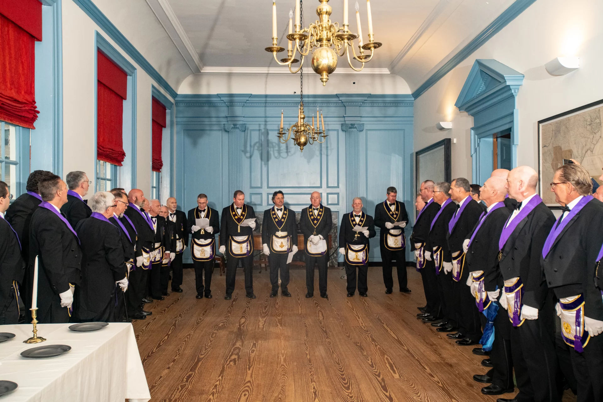 Group of Masons standing on either side of a large room with Grand Lodge Officers in the center.