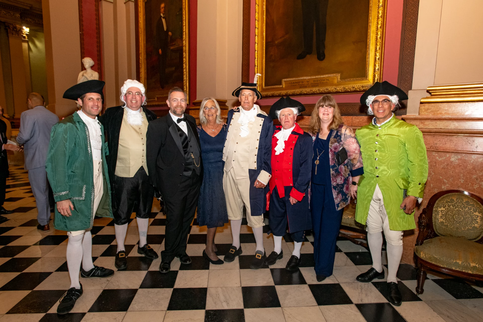 Group of men and women standing together in a hall at the Masonic Temple, many dressed in colonial outfits.