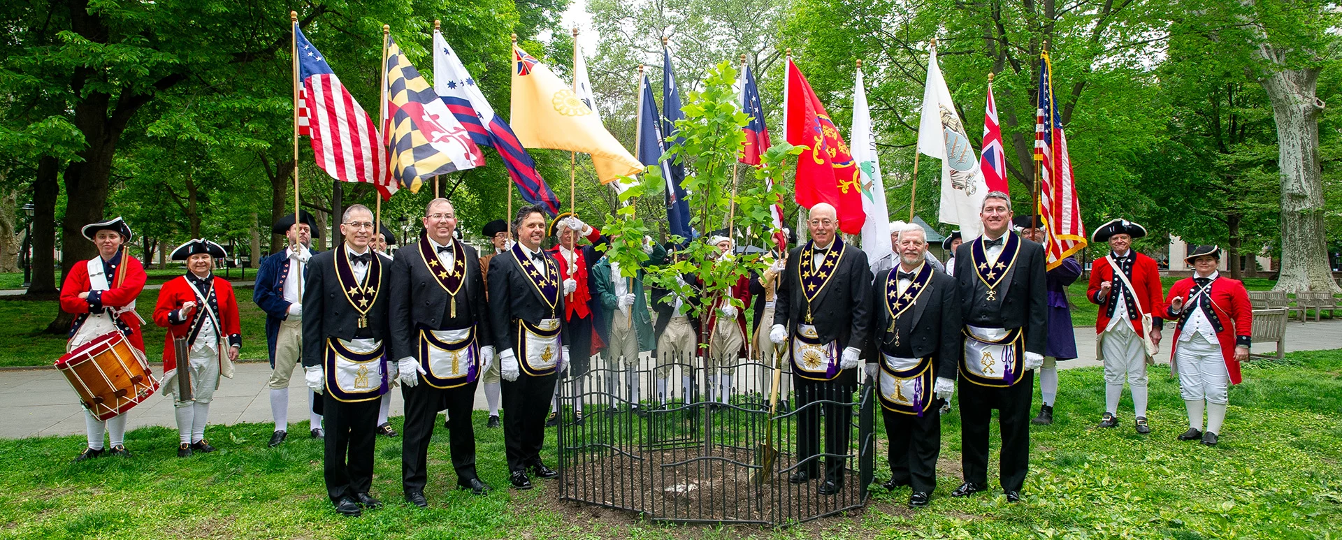 Grand Lodge Officers smiling while surrounding a newly planted Liberty Tree outdoors.