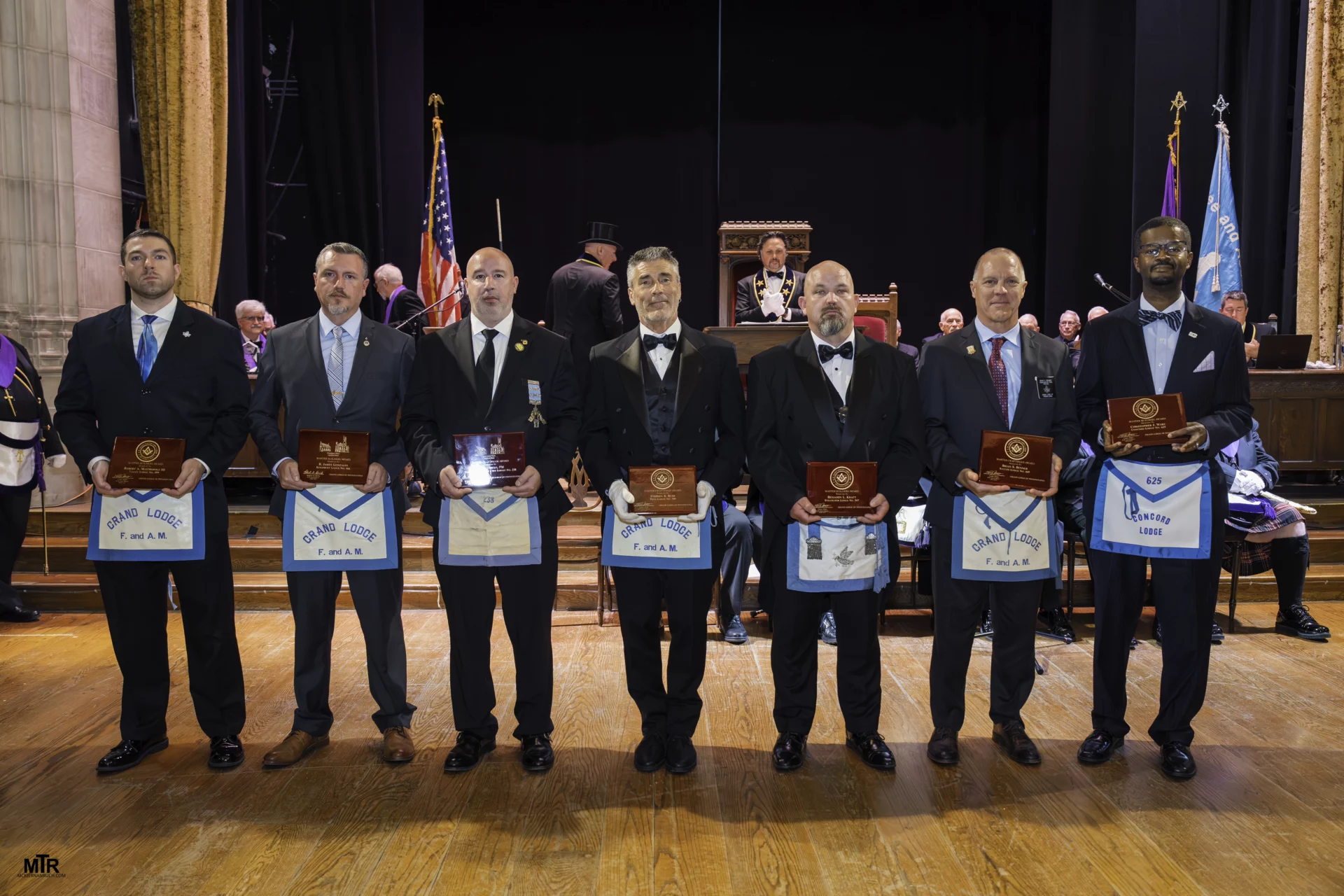 Smiling group of men dressed in Masonic attire, holding up awards.