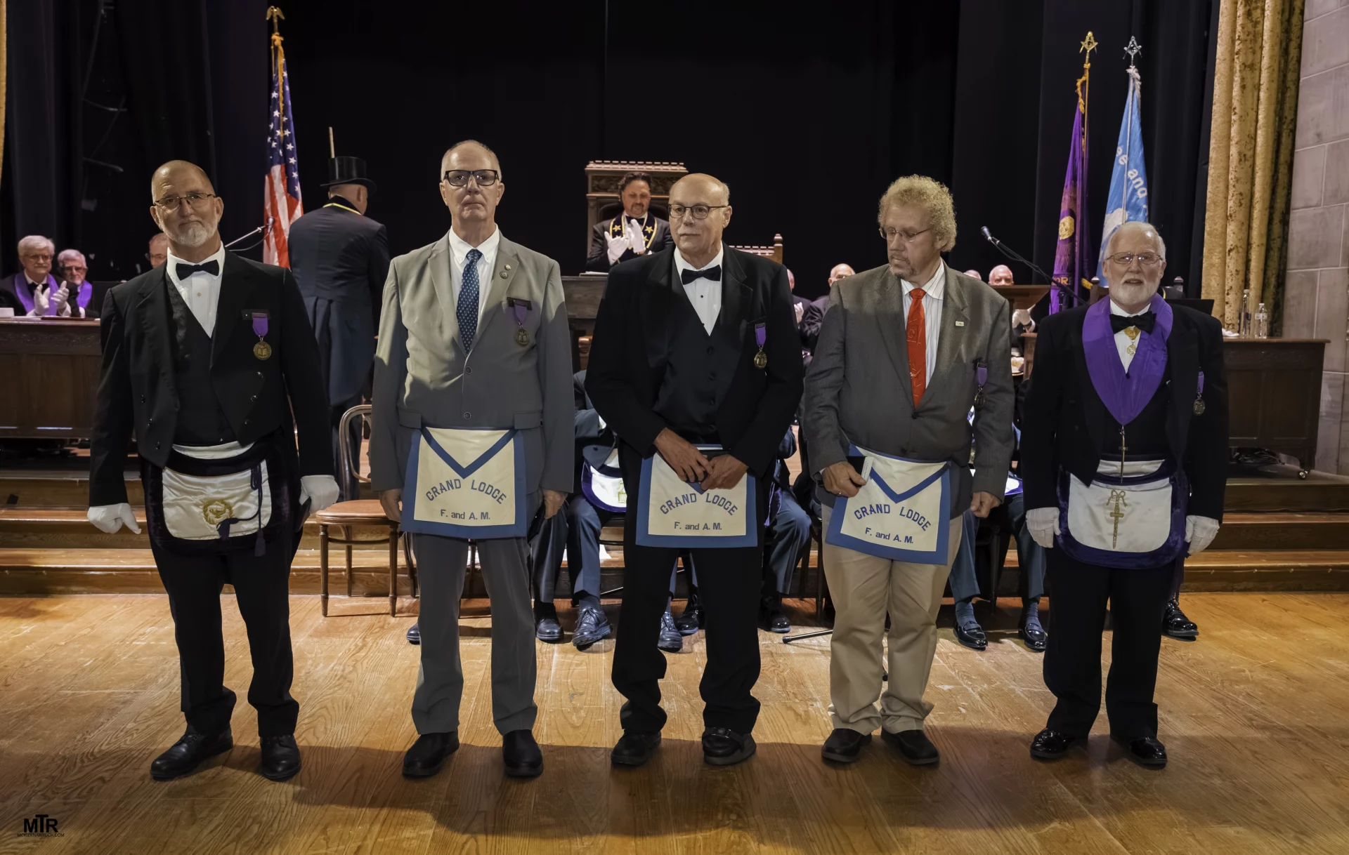 Smiling group of men in Masonic dress standing in a large room.