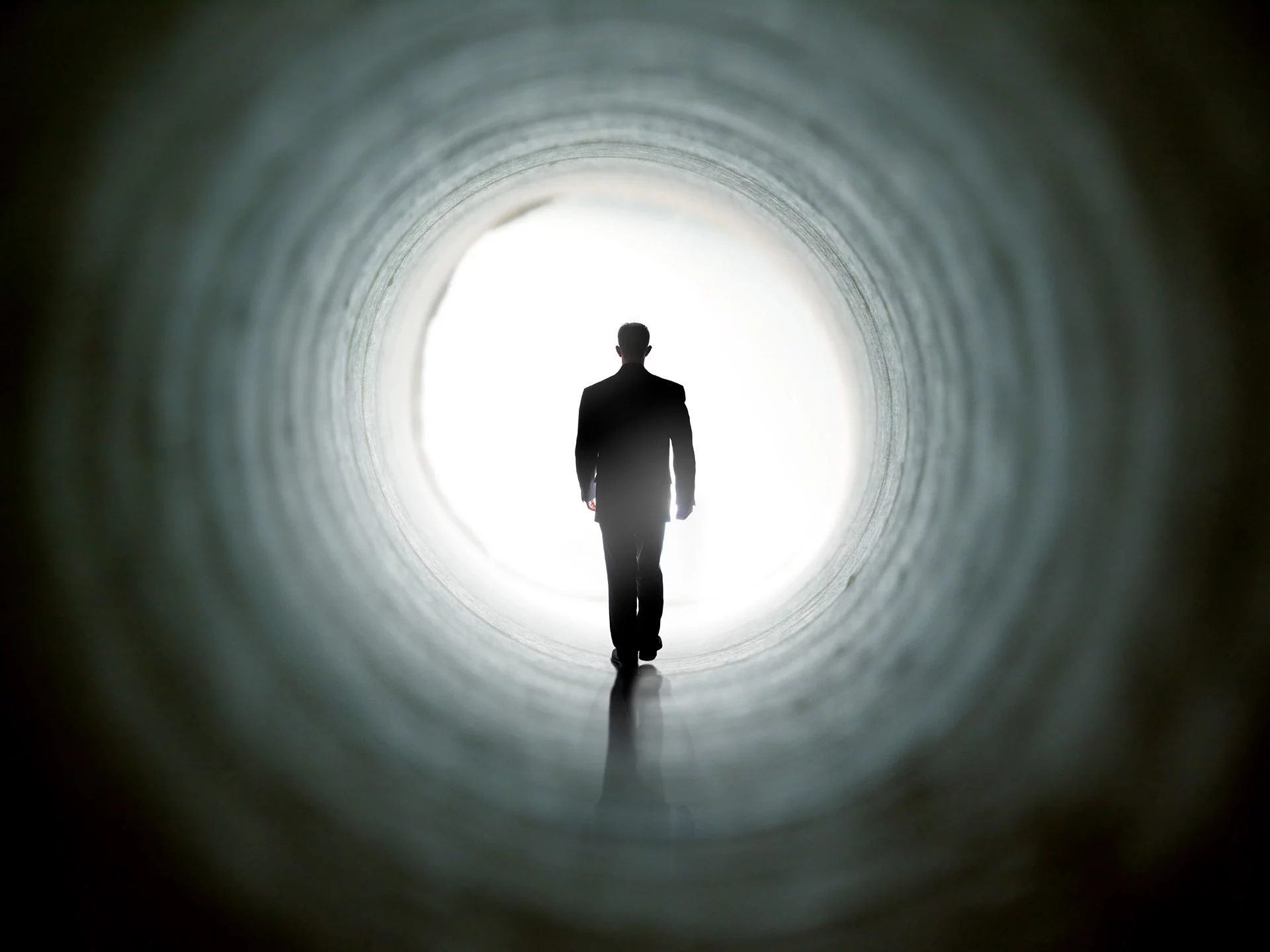 Dark outline of a man walking through a round structure with light behind him.