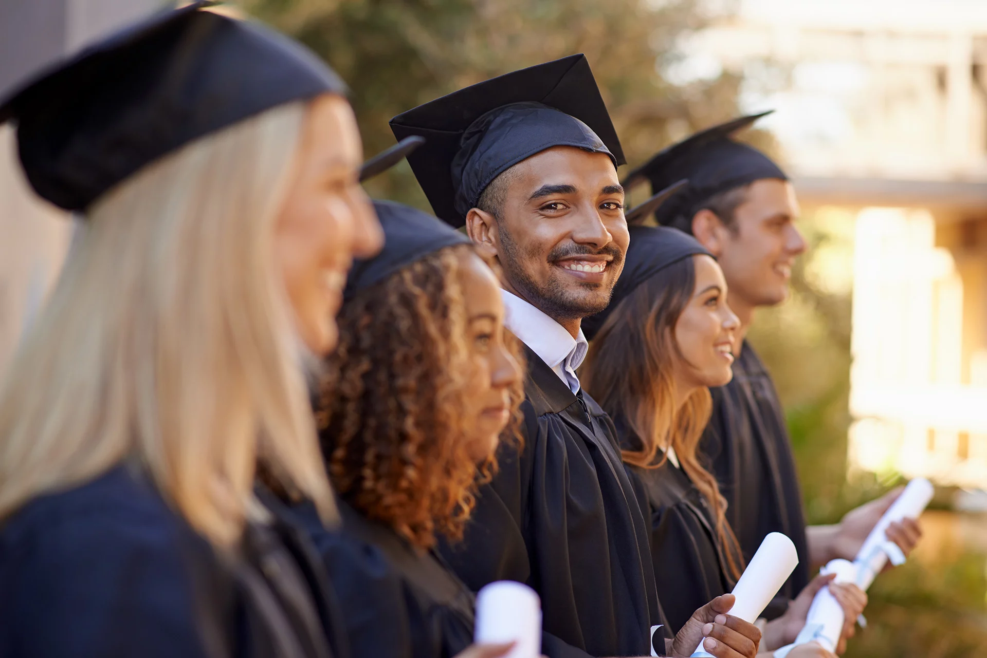 Smiling group of graduating students holding their diplomas while seated outdoors.