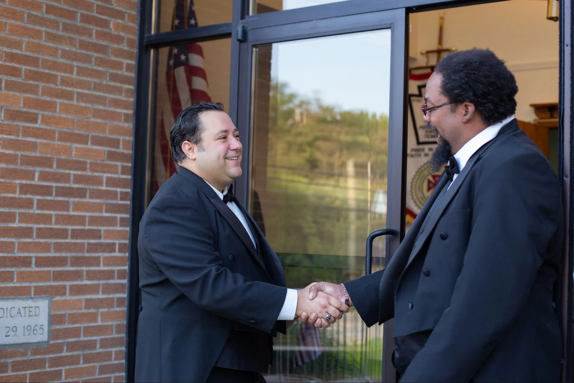 Smiling men shaking hands at a lodge doorway.