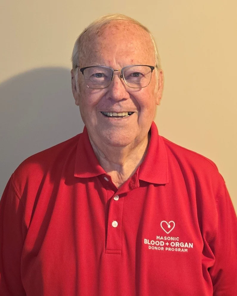 Smiling senior man with glasses wearing a red Masonic Blood + Organ Donor Program shirt.