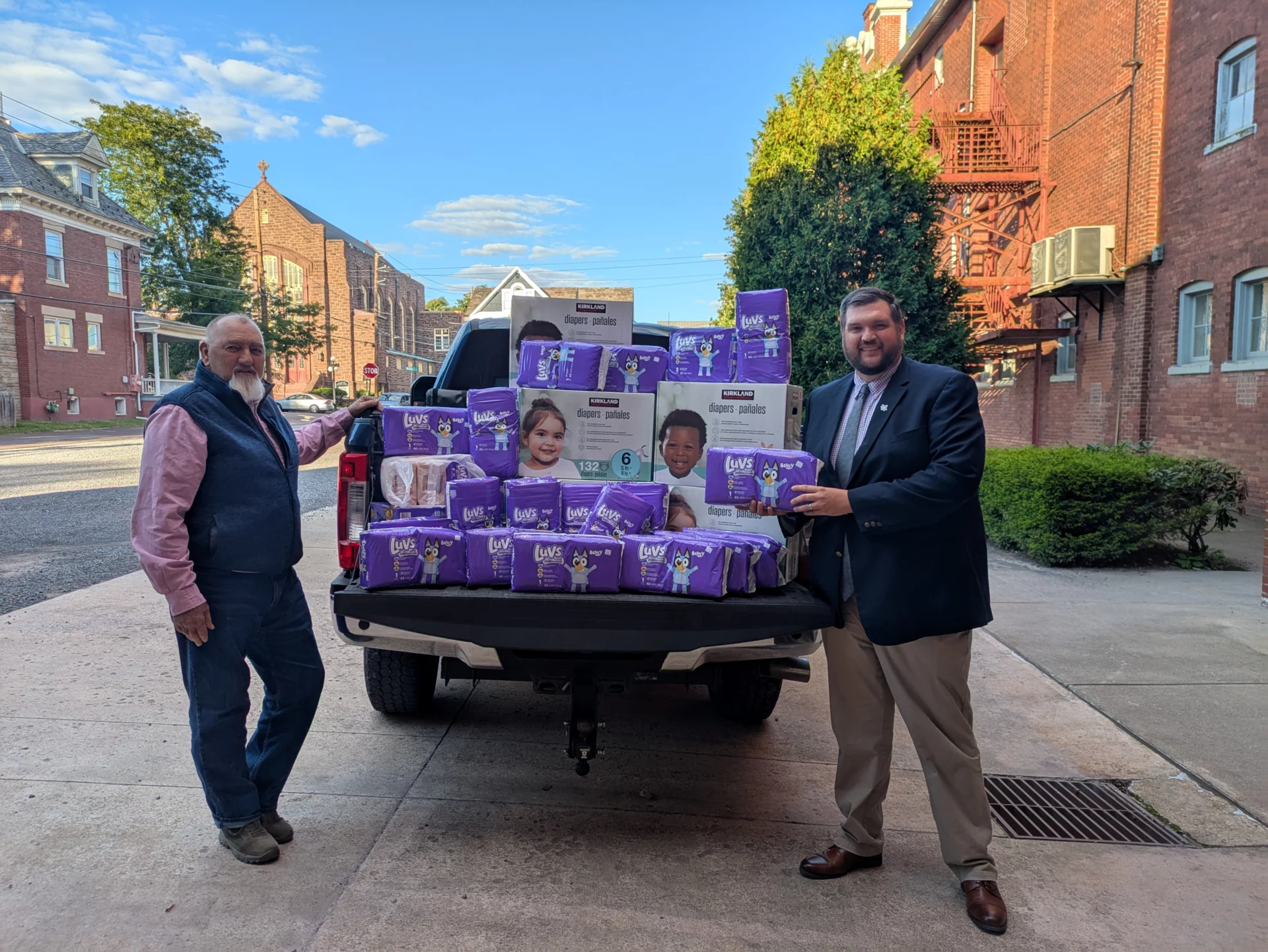 Two smiling Masons on either side of a pickup truck loaded with baby diapers.