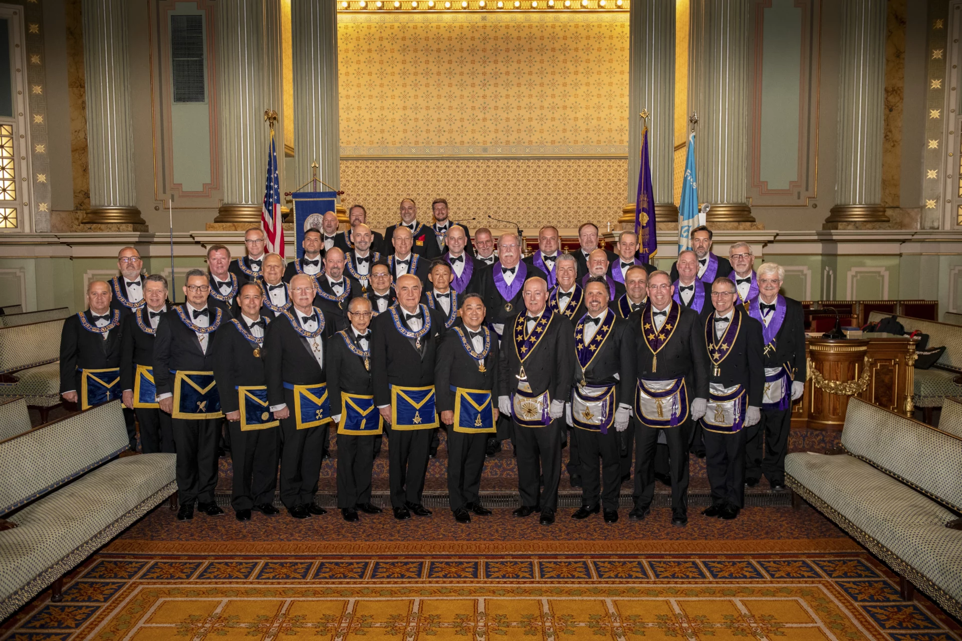 Smiling group of Masons, including Grand Lodge Officers, standing in an ornate lodge room.