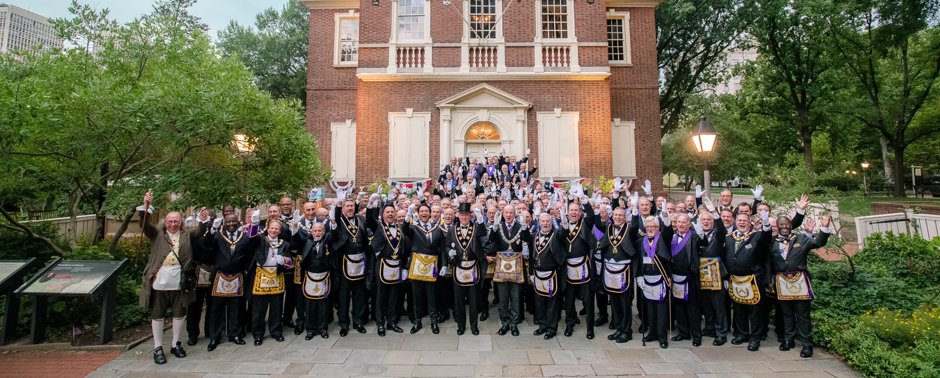 Smiling group of Masons with their arms up in front of a historic brick building.