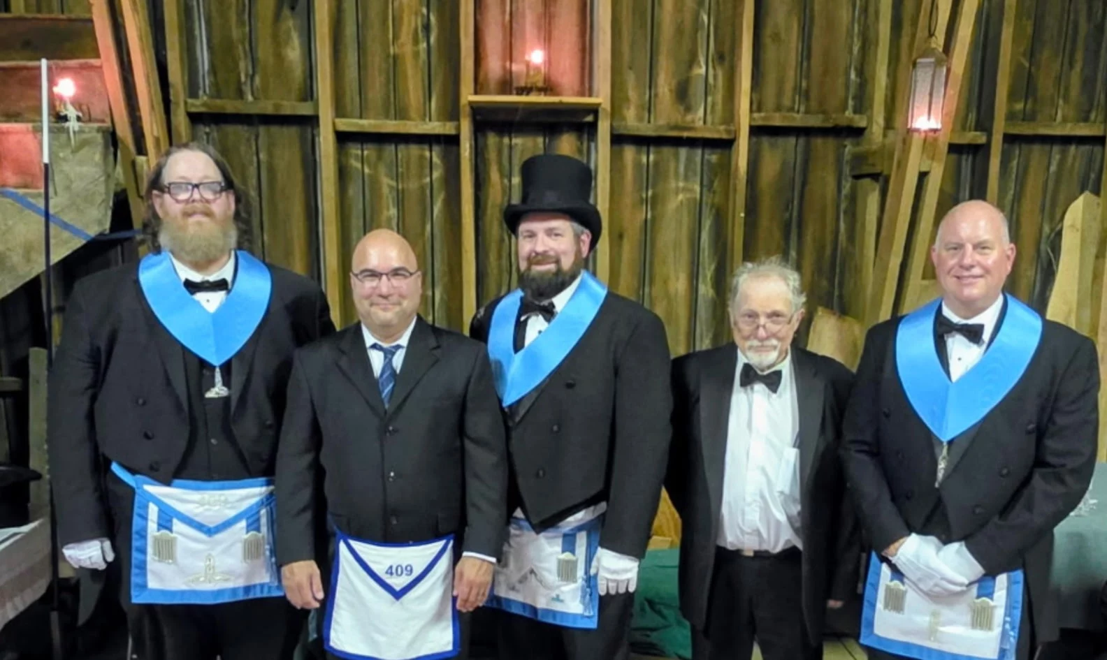 image002 Masons standing together against a rustic, wood background illuminated by candles and lanterns.